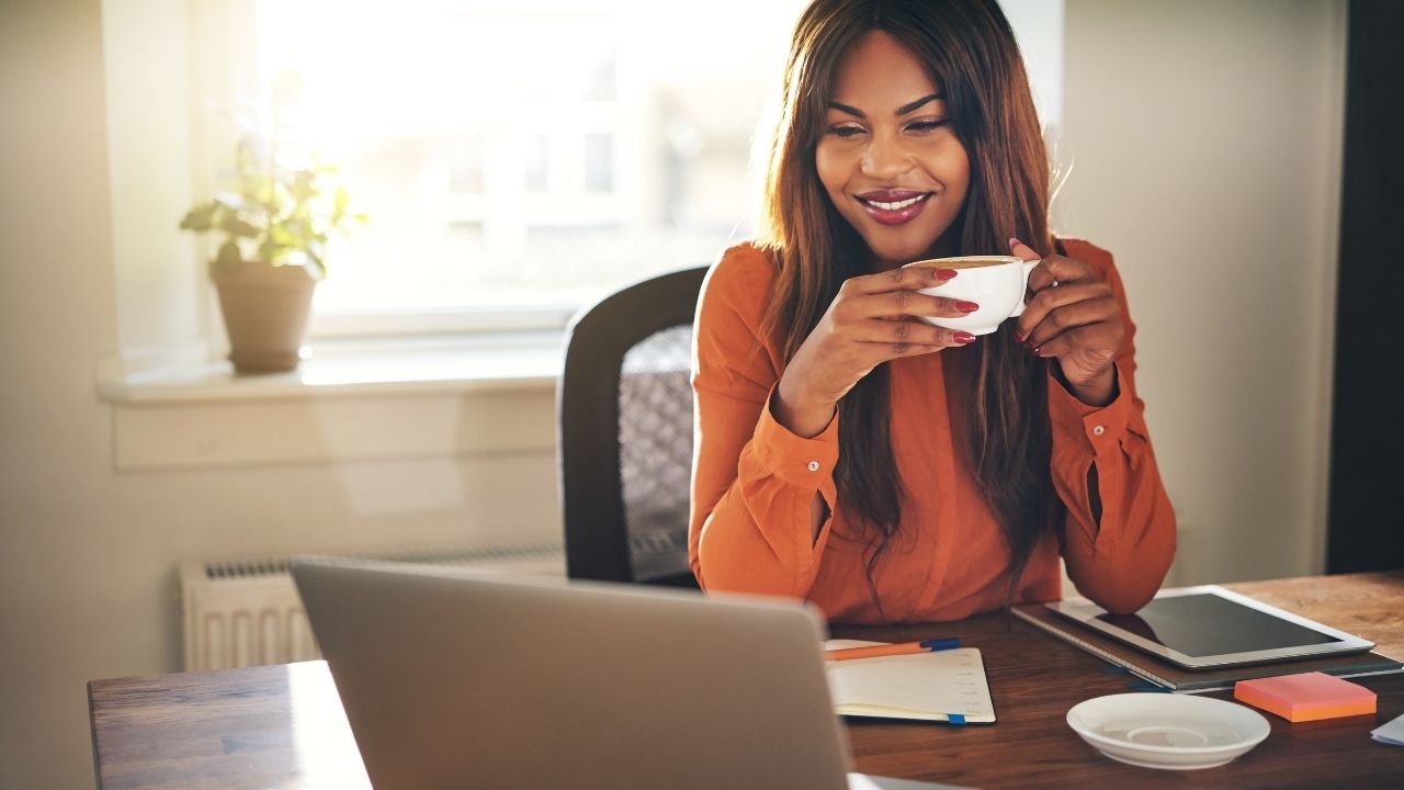 picture of a woman holding coffee looking at a laptop